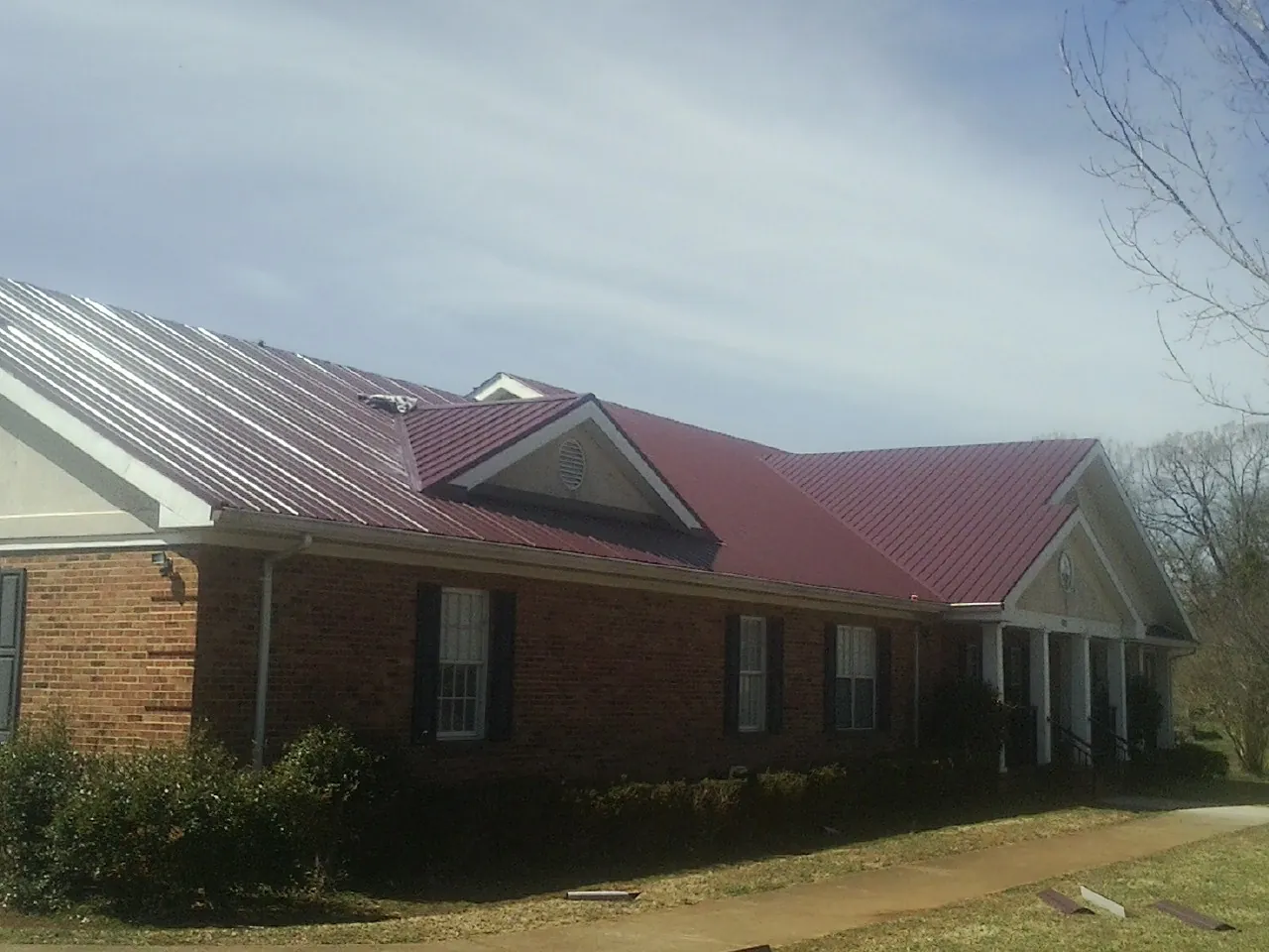 Red metal roof with gabled entries on a long brick building, from a Hail Damage Roof Repair job in Lopez Island