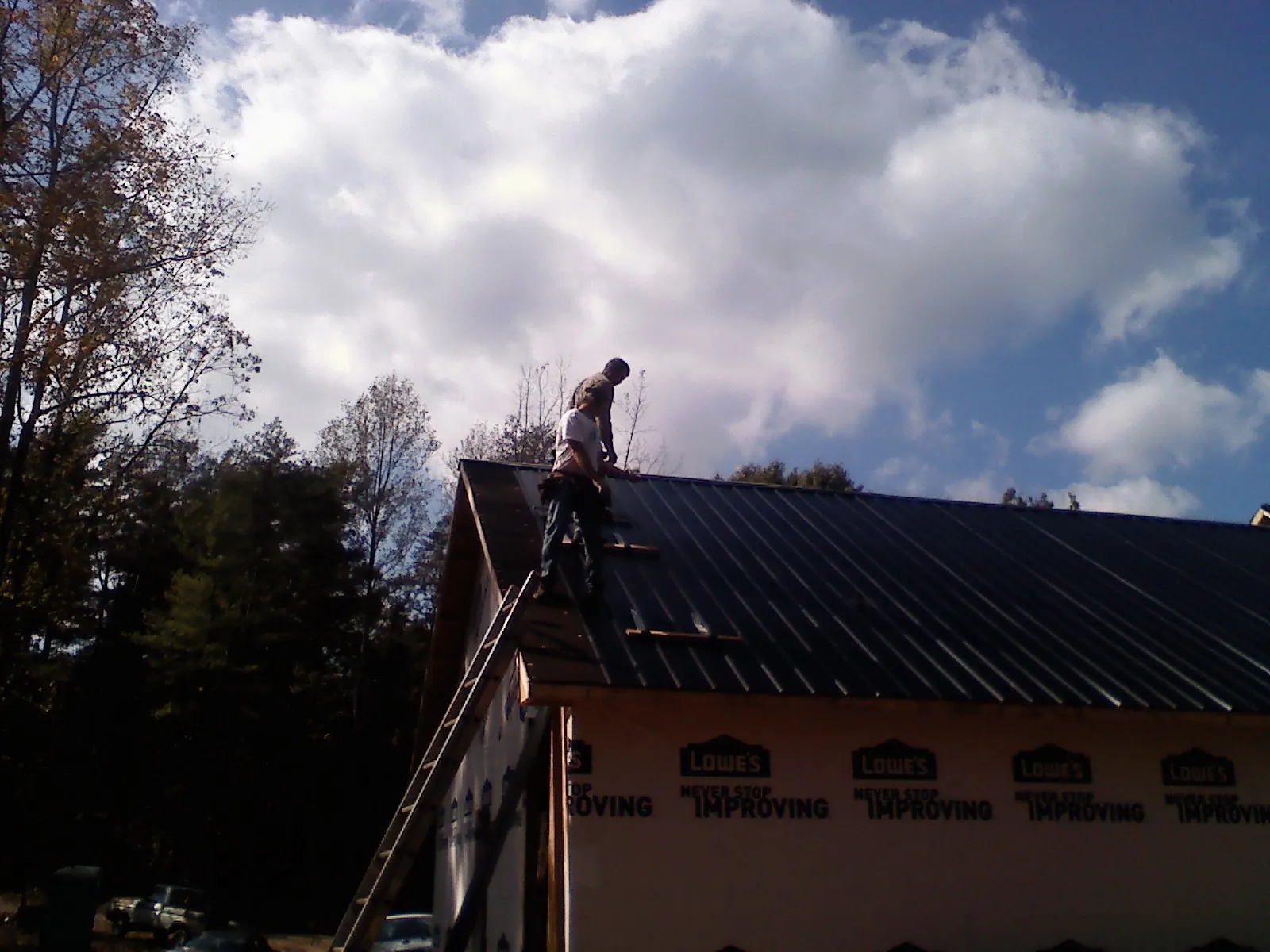 Roofer fastening dark metal panels high against a cloudy sky, from a Roof Inspection job in Lopez Island